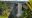 Thundering waterfall spilling over flat topped sandstone cliff with heavily forested jungle surrounding it
