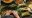 Close up of man's hands rolling a palm fond around food with finished parcels tied with raffia and bowls of meat sitting off to one side