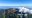 A stratovolcano featuring four craters with low cumulus clouds sitting over one side. It's rim and sides are covered in green coffee plantations